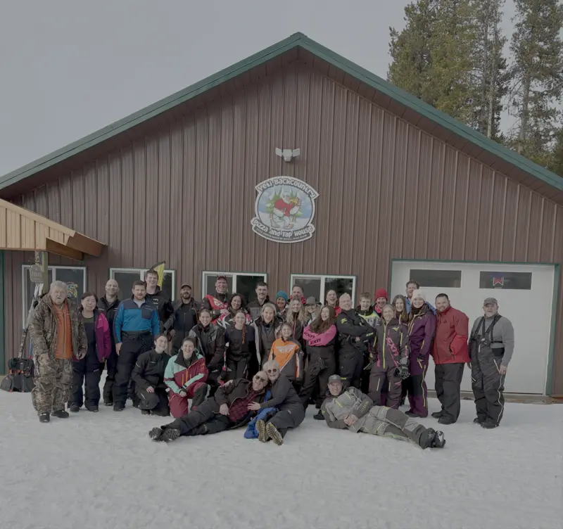 Post-ride group shot at Yeti Backcountry Pizza and Tap House — about three dozen riders in snowmobile gear stacked three rows deep in the snow, a few sprawled out front.